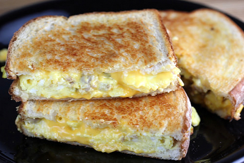 Egg and sausage grilled cheese sandwiches sliced and stacked on a black plate.