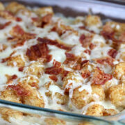 Tater tot casserole with melted cheese and crumbled bacon in a glass baking dish