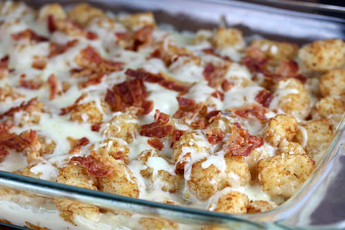 Tater tot casserole with melted cheese and crumbled bacon in a glass baking dish