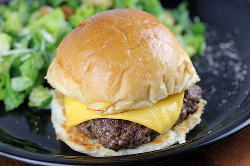 Garlic steakburger with melted cheese on a toasted bun served with a side salad.