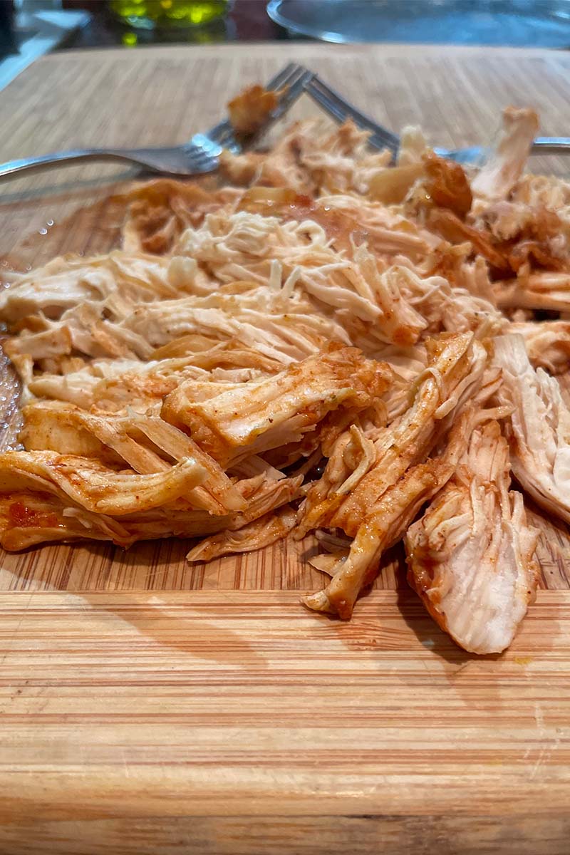 Shredded chicken on cutting board with two forks.