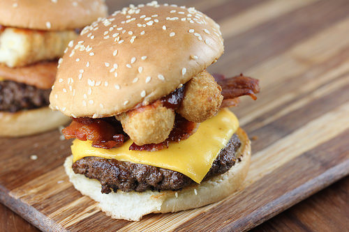 Mozzarella stick cheeseburger with bacon and beef patty on wooden surface