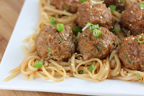 Juicy Asian pork meatballs garnished with green onions over noodles