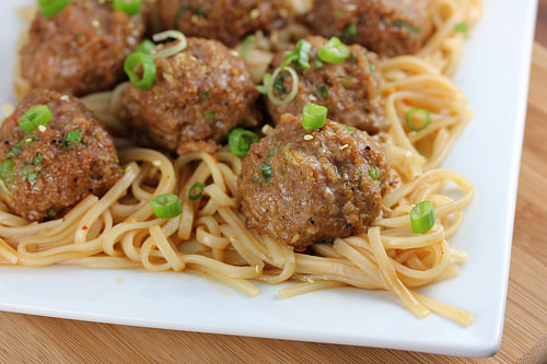 Juicy Asian pork meatballs garnished with green onions over noodles