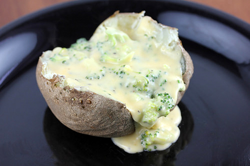 Baked potato topped with broccoli cheese sauce on a black plate