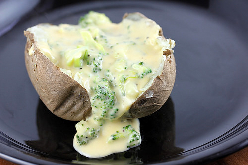 Baked potato topped with broccoli cheese sauce on a black plate