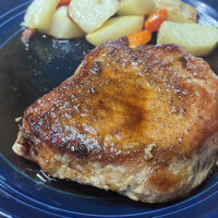 Prepared balsamic pork chop on plate with roasted vegetables.