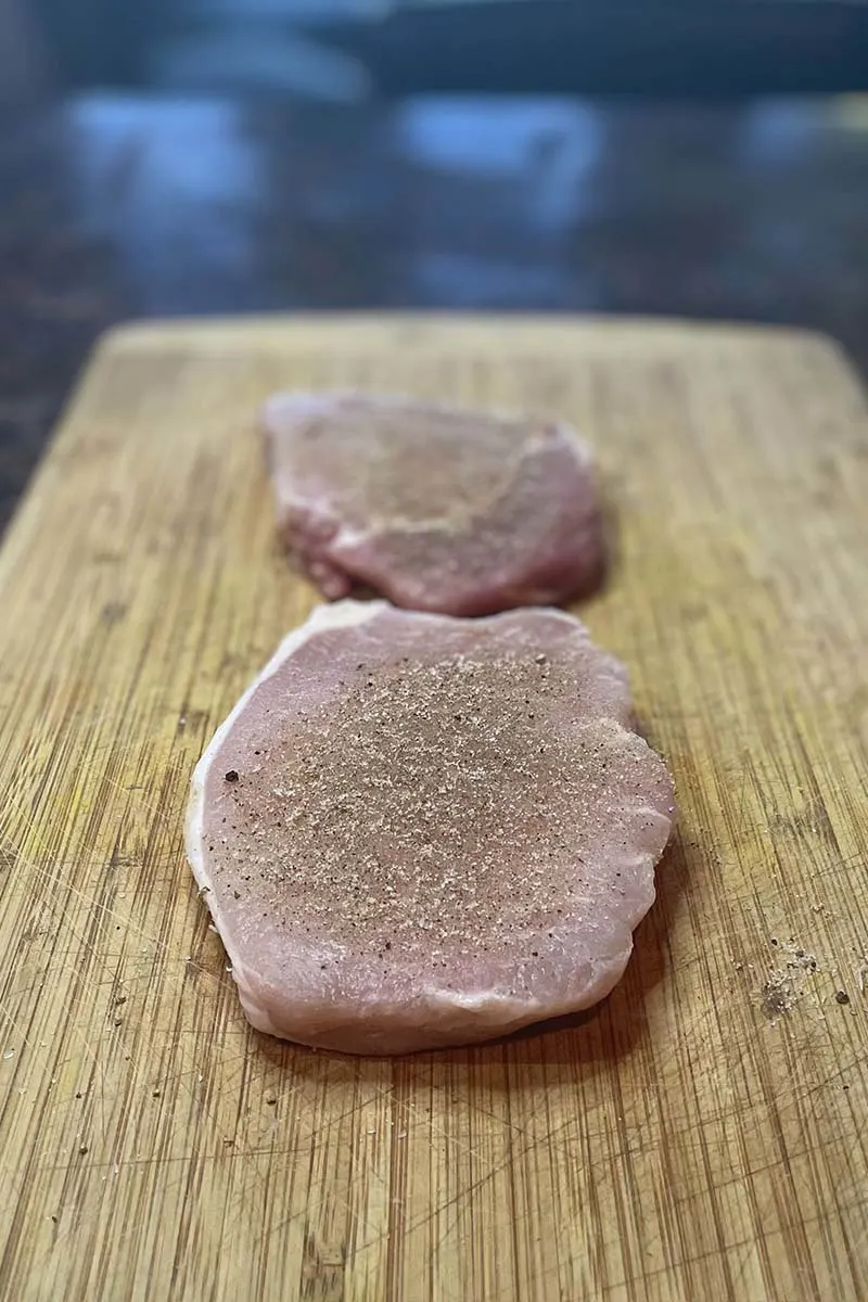 Raw pork loin chops with seasoning on cutting board.