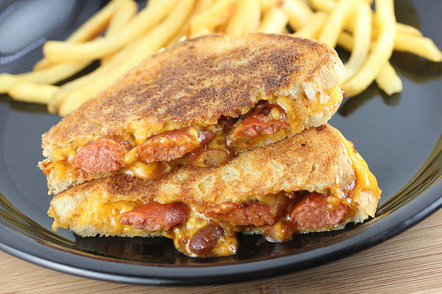 Grilled cheese sandwich stuffed with chili, sliced hot dogs, and melted cheddar served with fries