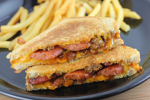 Grilled cheese sandwich stuffed with chili, sliced hot dogs, and melted cheddar served with fries