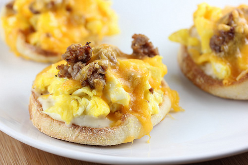 English muffin halves topped with eggs, sausage, and melted cheddar cheese on a white plate