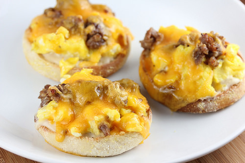 English muffin halves topped with eggs, sausage, and melted cheddar cheese on a white plate