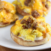 English muffin halves topped with eggs, sausage, and melted cheddar cheese on a white plate