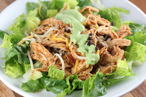 Chicken and black bean taco salad in a white bowl with lettuce and cheese