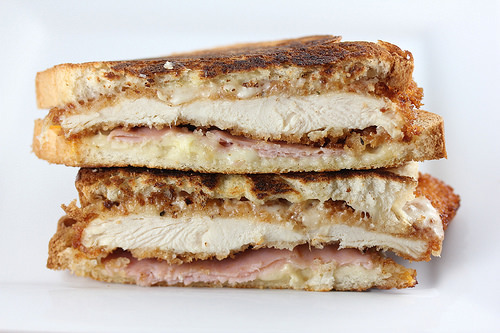 Grilled cheese sandwich stuffed with crispy chicken, ham, and melted cheese, cut in half