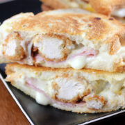Grilled cheese sandwich stuffed with crispy chicken, ham, and melted cheese, cut in half