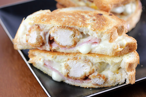 Grilled cheese sandwich stuffed with crispy chicken, ham, and melted cheese, cut in half