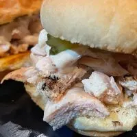 Close up view of grilled chicken sliders with white barbecue sauce.