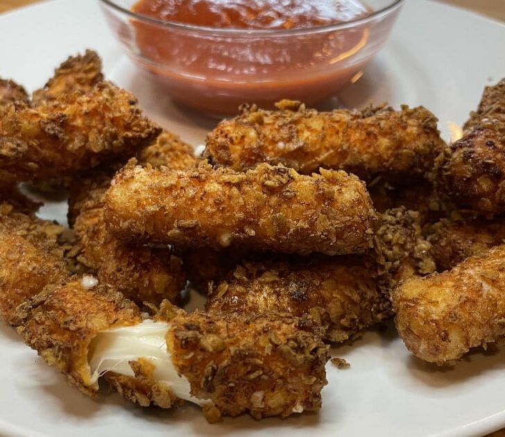 Doritos coated mozzarella sticks on a plate with marinara sauce.