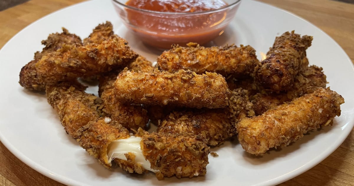 Doritos coated mozzarella sticks on a plate with marinara sauce.