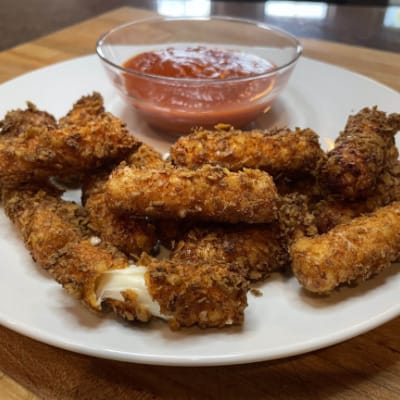 Doritos coated mozzarella sticks on a plate with marinara sauce.