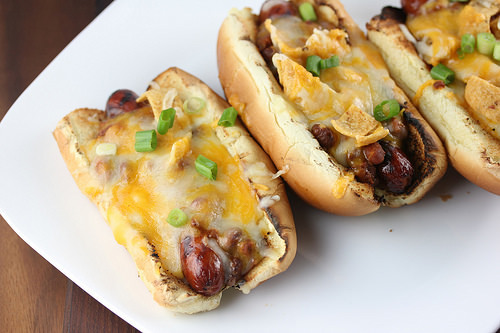 Frito pie hot dogs on a white plate with melted cheese and green onions
