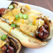 Frito pie hot dogs on a white plate with melted cheese and green onions