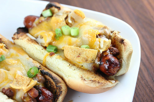 Frito pie hot dogs on a white plate with melted cheese and green onions