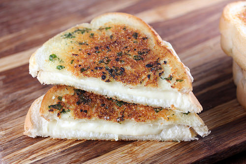 Toasted garlic bread grilled cheese on a wooden board with gooey cheese filling