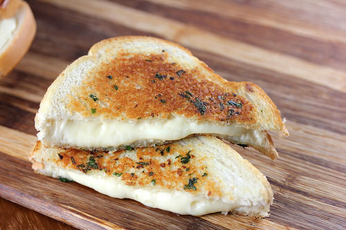 Toasted garlic bread grilled cheese on a wooden board with gooey cheese filling