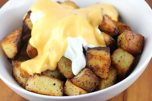 Cheesy fiesta potatoes topped with nacho cheese and sour cream in a white bowl