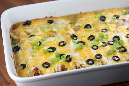Ground beef enchiladas topped with melted cheese black olives and green onions in baking dish