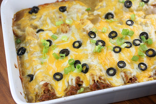 Ground beef enchiladas topped with melted cheese black olives and green onions in baking dish