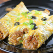 Ground beef enchiladas topped with melted cheese black olives and green onions in baking dish