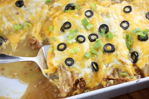 Ground beef enchiladas topped with melted cheese black olives and green onions in baking dish