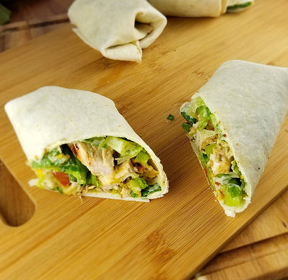 Sliced burrito filled with grilled chicken, lettuce, tomato, and avocado on a wooden board