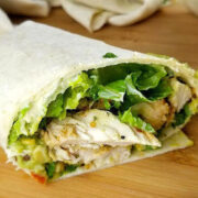 Sliced burrito filled with grilled chicken, lettuce, tomato, and avocado on a wooden board