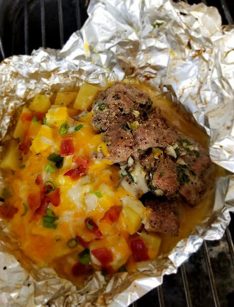Steak and potato foil packet with melted cheese, bacon, and green onions