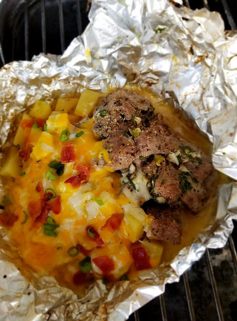 Steak and potato foil packet with melted cheese, bacon, and green onions