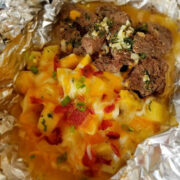 Steak and potato foil packet with melted cheese, bacon, and green onions