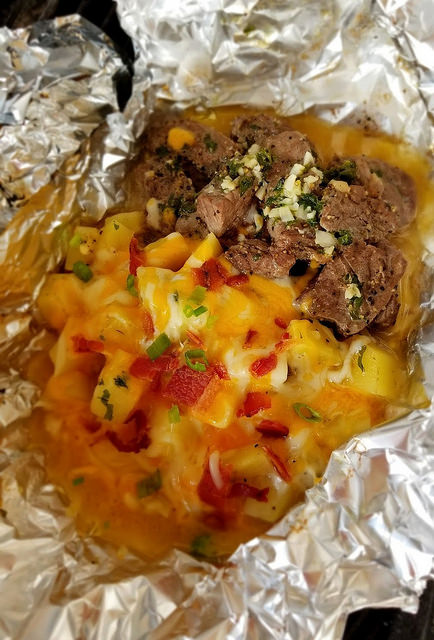 Steak and potato foil packet with melted cheese, bacon, and green onions