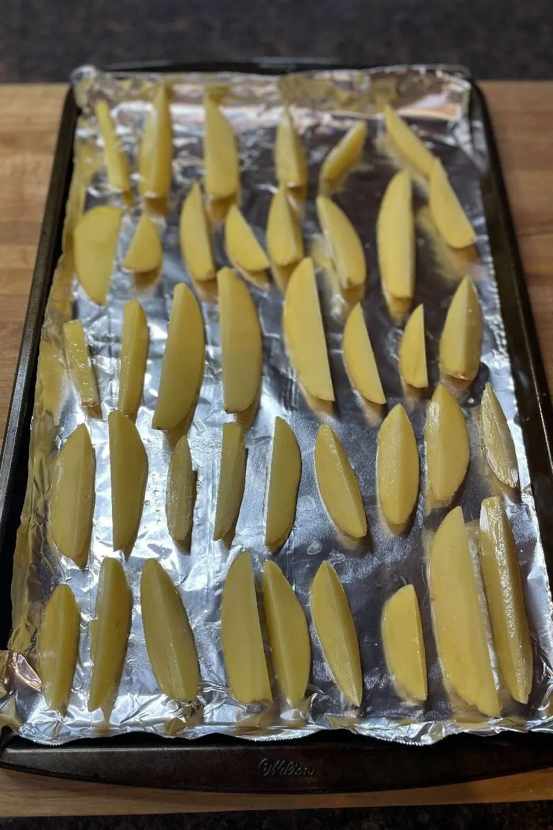 Potato wedges arranged on baking sheet.