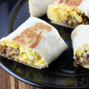 Breakfast burrito cut in half with scrambled eggs, sausage, and cheese on a black plate