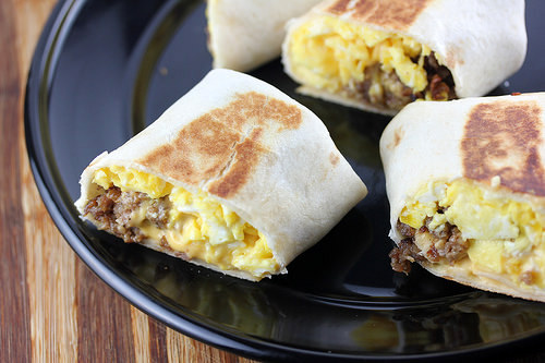 Breakfast burrito cut in half with scrambled eggs, sausage, and cheese on a black plate