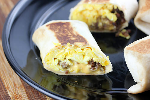 Breakfast burrito cut in half with scrambled eggs, sausage, and cheese on a black plate