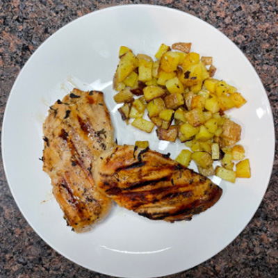 Top view of artisan grilled chicken on plate with potatoes.