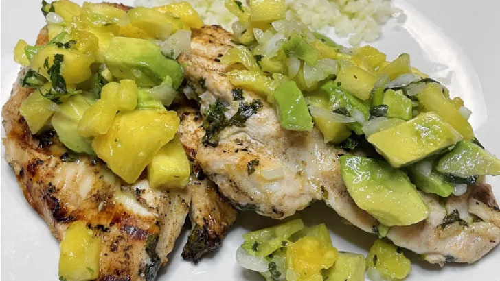 Top view of grilled chicken with avocado salsa on plate with rice.