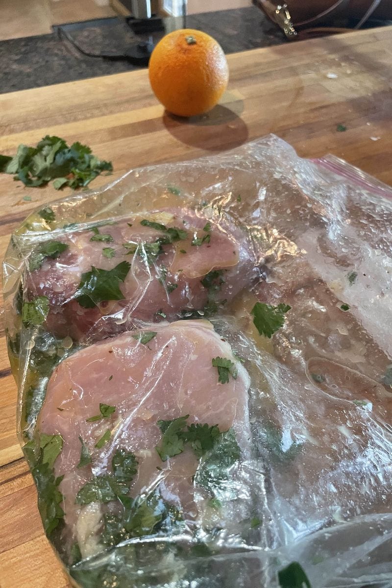 Cuban marinade and pork chops inside resealable bag on cutting board.