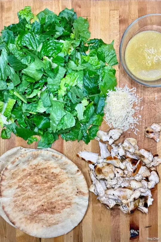 Romaine lettuce, chicken, cheese, salad dressing on cutting board.