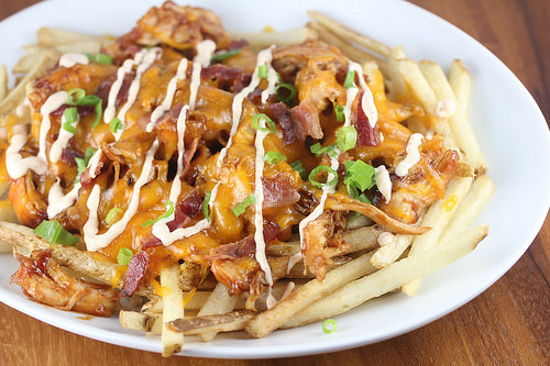 BBQ chicken fries with melted cheese, bacon, and scallions on a white plate